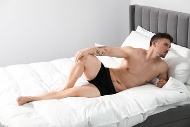 Photo of Young man in stylish black underwear on bed indoors