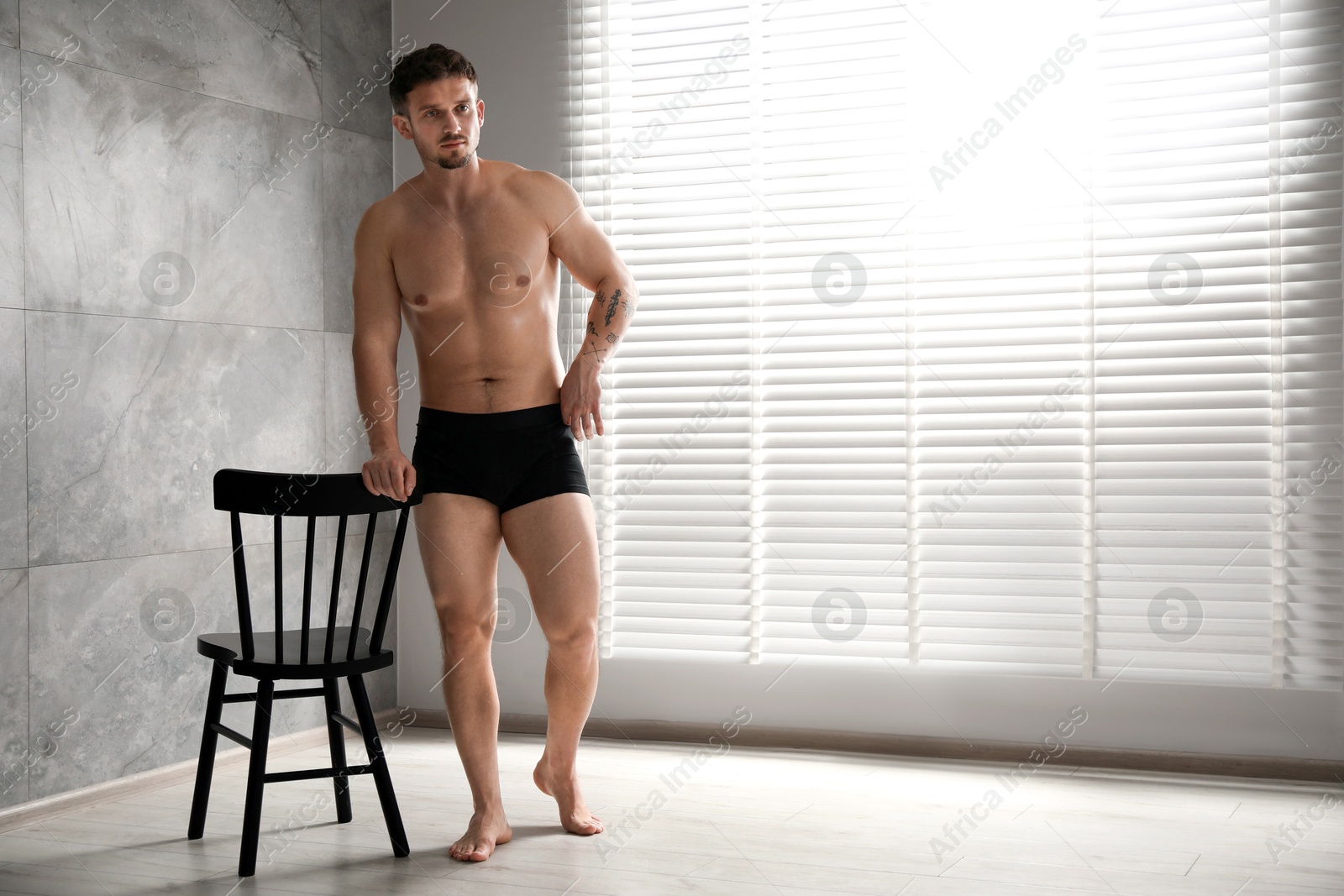 Young man in stylish black underwear near chair indoors. Space for text Photo of Young man in stylish black underwear near chair indoors. Space for text