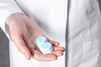 Photo of Doctor holding case with contact lenses on grey background, closeup