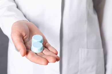 Photo of Doctor holding case with contact lenses on grey background, closeup