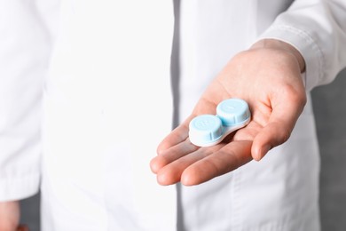 Photo of Doctor holding case with contact lenses on grey background, closeup
