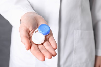 Photo of Doctor holding case with contact lenses on grey background, closeup