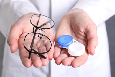 Photo of Doctor holding case with contact lenses and glasses on grey background, closeup