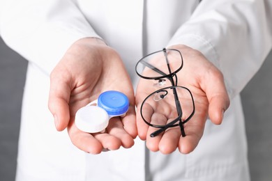 Photo of Doctor holding case with contact lenses and glasses on grey background, closeup
