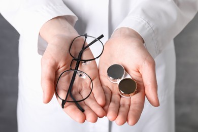 Photo of Doctor holding case with contact lenses and glasses on grey background, closeup