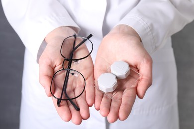 Photo of Doctor holding case with contact lenses and glasses on grey background, closeup