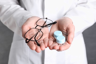 Photo of Doctor holding case with contact lenses and glasses on grey background, closeup