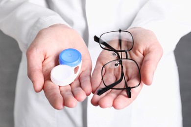 Photo of Doctor holding case with contact lenses and glasses on grey background, closeup