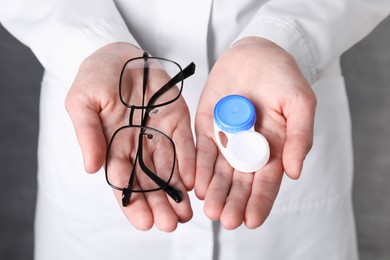 Photo of Doctor holding case with contact lenses and glasses on grey background, closeup