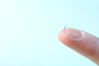 Photo of Woman with contact lens on light blue background, closeup. Space for text