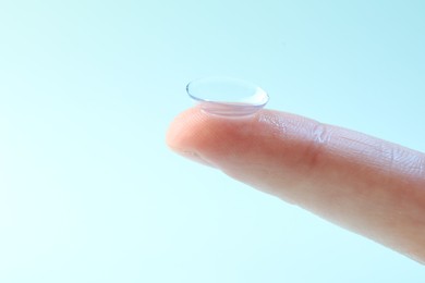 Photo of Woman with contact lens on light blue background, closeup. Space for text