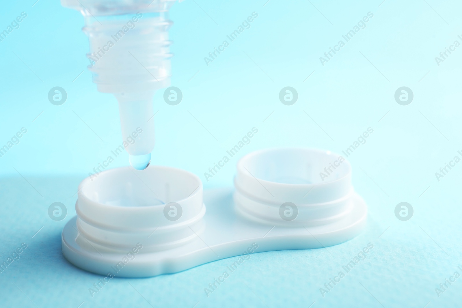 Dripping solution into case with contact lenses on light blue background, closeup Photo of Dripping solution into case with contact lenses on light blue background, closeup