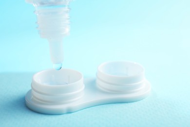 Photo of Dripping solution into case with contact lenses on light blue background, closeup