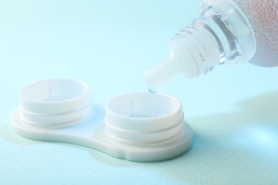 Photo of Dripping solution into case with contact lenses on light blue background, closeup