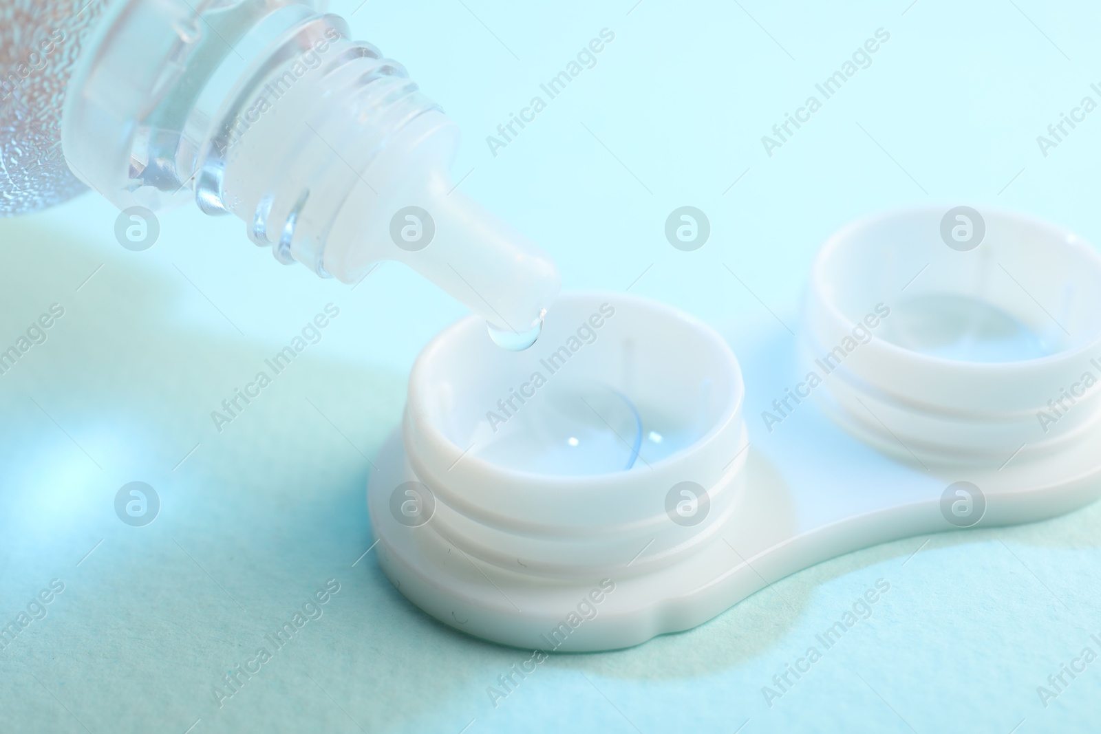 Dripping solution into case with contact lenses on light blue background, closeup Photo of Dripping solution into case with contact lenses on light blue background, closeup