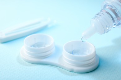 Photo of Dripping solution into case with contact lenses on light blue background, closeup