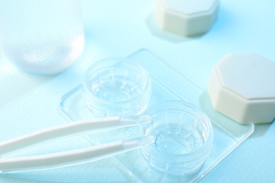 Photo of Case with contact lenses and tweezers on light blue background, closeup