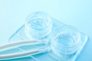 Photo of Case with contact lenses and tweezers on light blue background, closeup