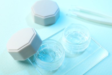 Photo of Case with contact lenses and tweezers on light blue background, closeup