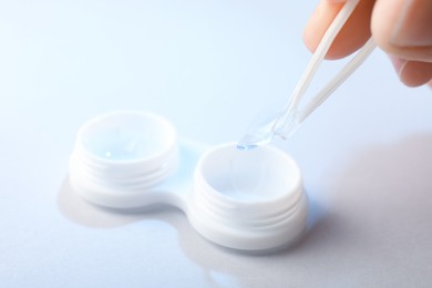 Photo of Woman taking contact lens out of case with tweezers on white background, closeup