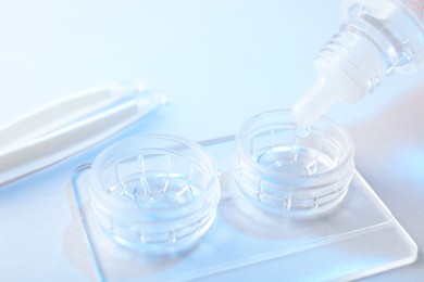 Photo of Dripping solution into case with contact lenses on light background, closeup