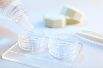 Photo of Dripping solution into case with contact lenses on light background, closeup