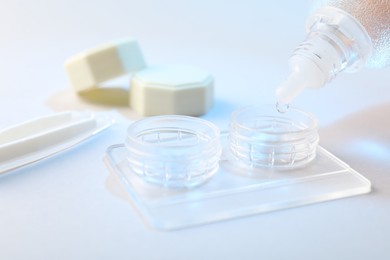 Photo of Dripping solution into case with contact lenses on light background, closeup