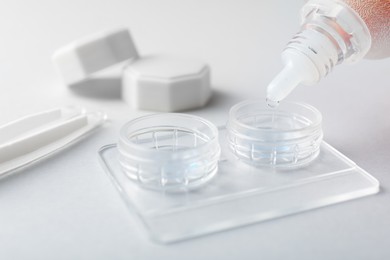 Photo of Dripping solution into case with contact lenses on light background, closeup