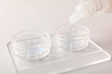 Photo of Dripping solution into case with contact lenses on light background, closeup