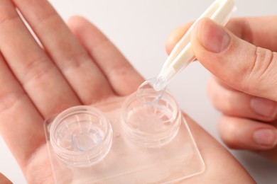 Photo of Woman taking contact lens out of case with tweezers on white background, closeup