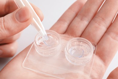 Photo of Woman taking contact lens out of case with tweezers on white background, closeup