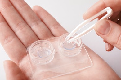 Photo of Woman taking contact lens out of case with tweezers on white background, closeup