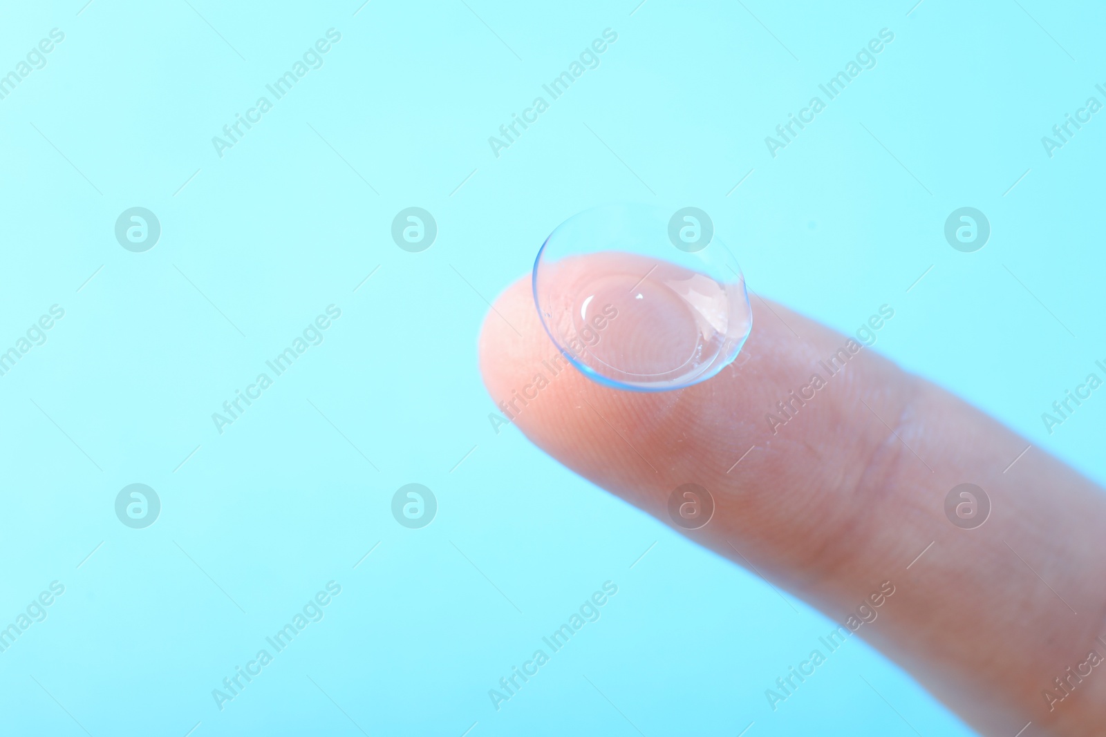 Woman with contact lens on light blue background, closeup. Space for text Photo of Woman with contact lens on light blue background, closeup. Space for text