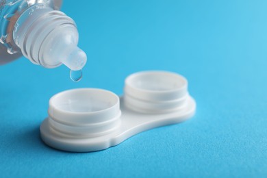 Photo of Dripping solution into case with contact lenses on light blue background, closeup. Space for text