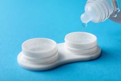 Photo of Dripping solution into case with contact lenses on light blue background, closeup. Space for text
