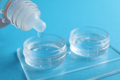 Photo of Dripping solution into case with contact lenses on light blue background, closeup