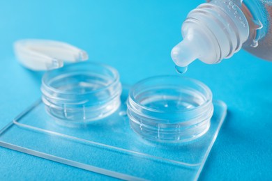 Photo of Dripping solution into case with contact lenses on light blue background, closeup