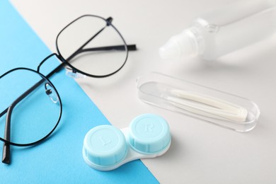Photo of Case with contact lenses, glasses, tweezers and liquid solution on color background, closeup