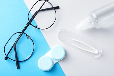 Photo of Case with contact lenses, glasses, tweezers and liquid solution on color background, flat lay