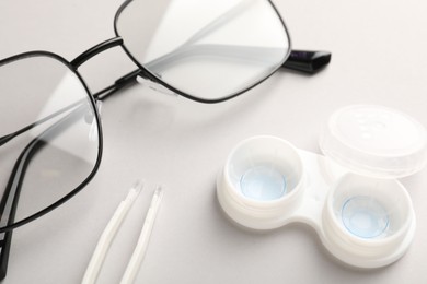 Photo of Case with contact lenses, tweezers and glasses on white background, closeup