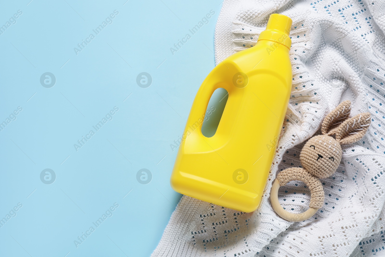 Bottle of fabric softener, toy and baby blanket on light blue background, flat lay. Space for text Photo of Bottle of fabric softener, toy and baby blanket on light blue background, flat lay. Space for text