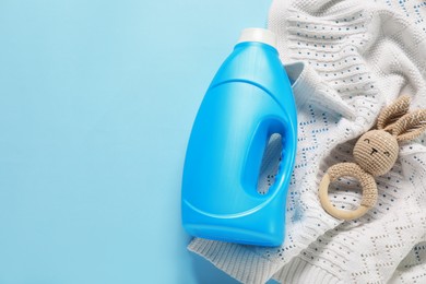 Photo of Bottle of fabric softener, toy and baby blanket on light blue background, flat lay. Space for text