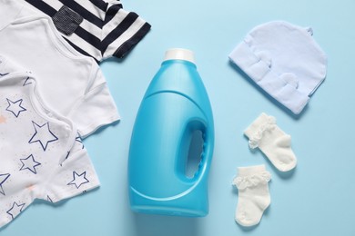 Photo of Bottle of fabric softener and baby clothes on light blue background, flat lay