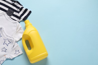 Photo of Bottle of fabric softener and baby clothes on light blue background, flat lay. Space for text