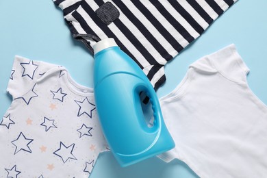 Photo of Bottle of fabric softener and baby clothes on light blue background, flat lay
