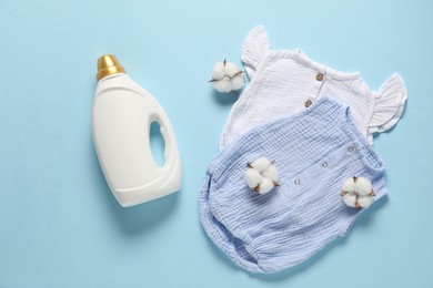 Photo of Bottle of fabric softener, cotton flowers and baby clothes on light blue background, flat lay