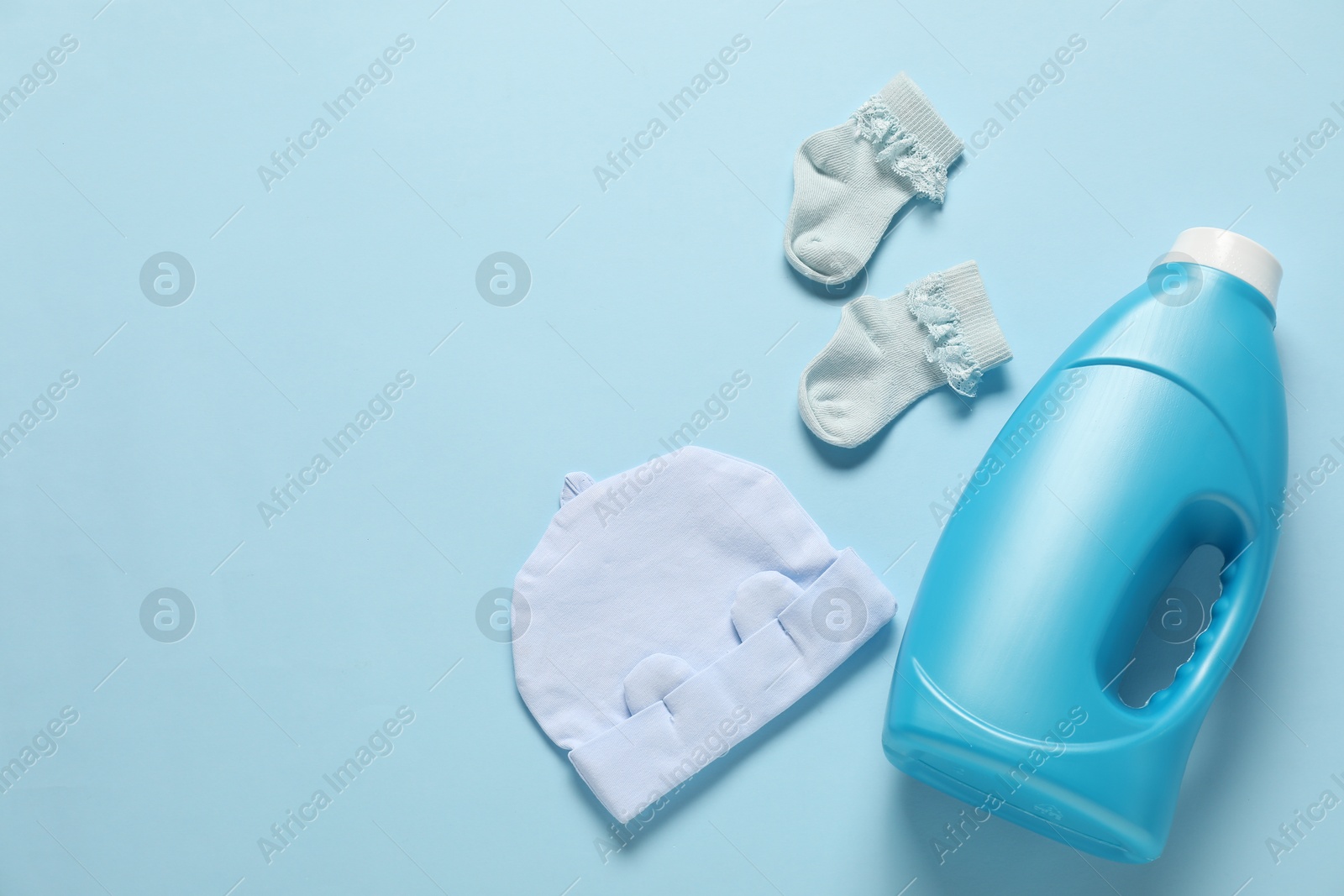 Bottle of fabric softener and baby clothes on light blue background, flat lay. Space for text Photo of Bottle of fabric softener and baby clothes on light blue background, flat lay. Space for text