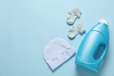 Photo of Bottle of fabric softener and baby clothes on light blue background, flat lay. Space for text