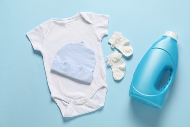 Photo of Bottle of fabric softener and baby clothes on light blue background, flat lay