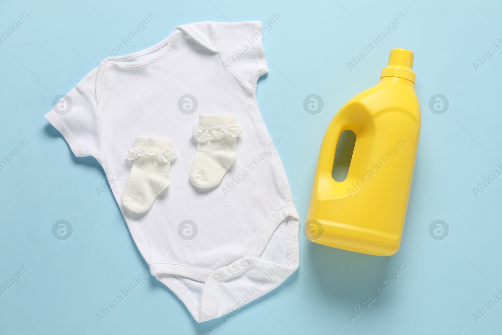 Bottle of fabric softener and baby clothes on light blue background, flat lay Photo of Bottle of fabric softener and baby clothes on light blue background, flat lay
